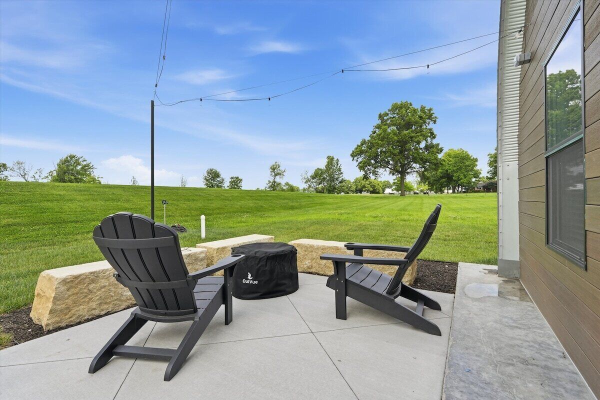 An outdoor patio with two Adirondack chairs, a black bag, and a string of lights.