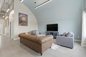 Ein modernes Wohnzimmer mit einem braunen Ledersofa, einem grauen Couch mit Muster, einem Flachbildfernseher und einem Poster an der Wand.