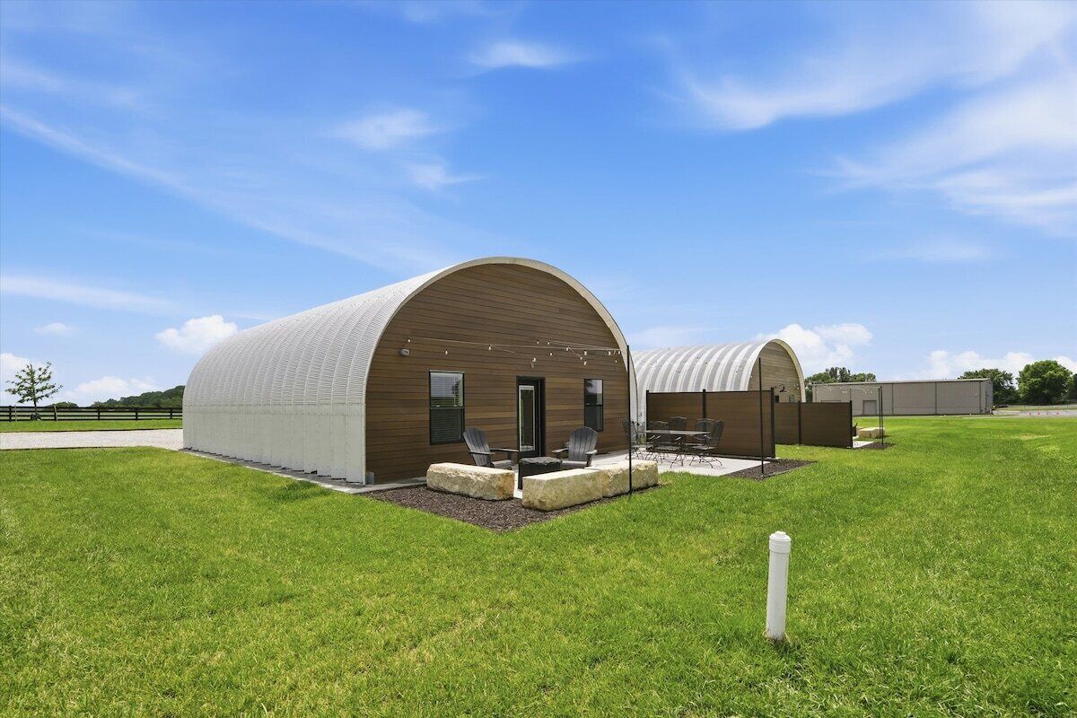 Un bâtiment moderne doté d’un toit incurvé, d’un patio aménagé avec des sièges et d’une pelouse bien entretenue.