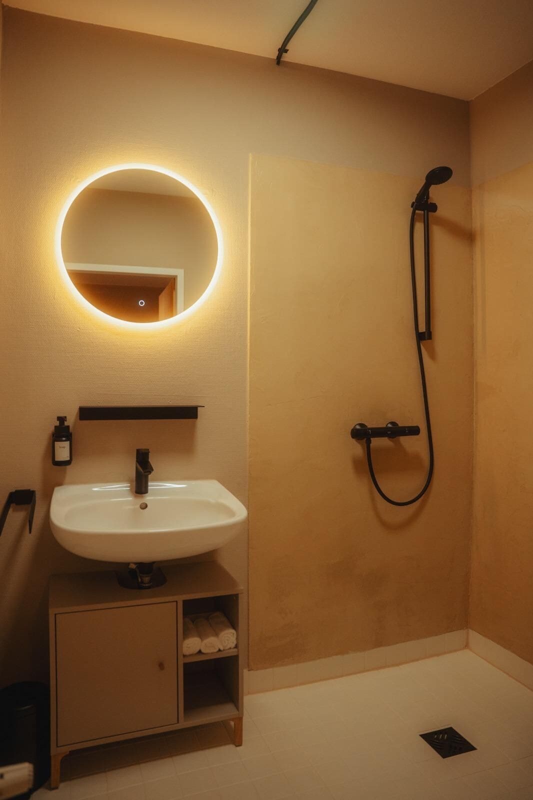 Ein Badezimmer mit rundem Spiegel, Waschbecken, Dusche und Handtuchhalter.
