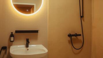 Ein Badezimmer mit rundem Spiegel, Waschbecken, Dusche und Handtuchhalter.