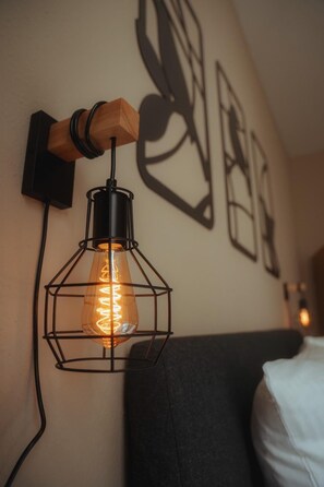 A wall-mounted light fixture with a wooden base and a metal frame, a bed with a white pillow, and abstract wall art. - City Apartment I Free Parking (Bielefeld)