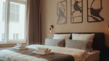 Ein ordentlich bezogenes Bett mit Kissen und Decke, eine Nachttischlampe und Vogelbilder an der Wand.