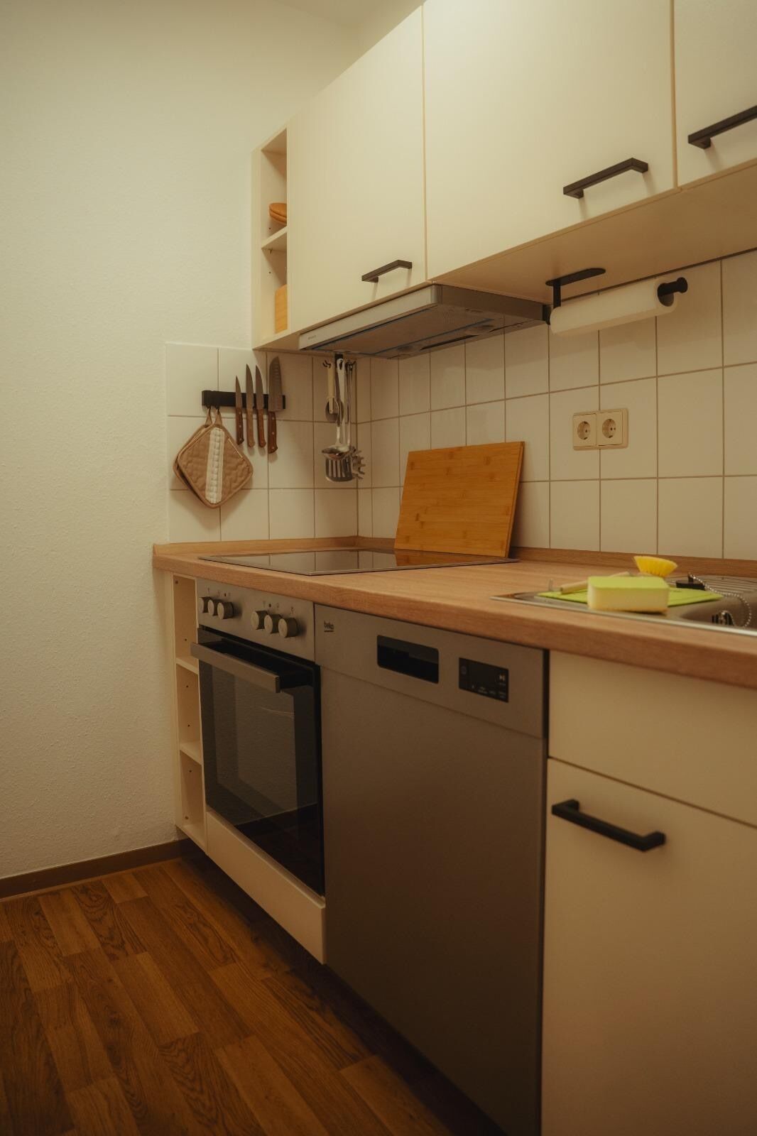 Eine Küche mit Holzausstattung, fest eingebautem Backofen, Geschirrspüler und einer Arbeitsplatte mit Schneidebrett und Schwamm.
