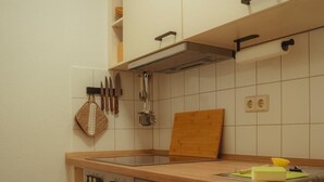 Uma cozinha com armários de madeira, forno embutido, lava-louças e bancada com tábua de corte e esponja.