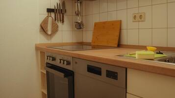 Eine Küche mit Holzausstattung, fest eingebautem Backofen, Geschirrspüler und einer Arbeitsplatte mit Schneidebrett und Schwamm.