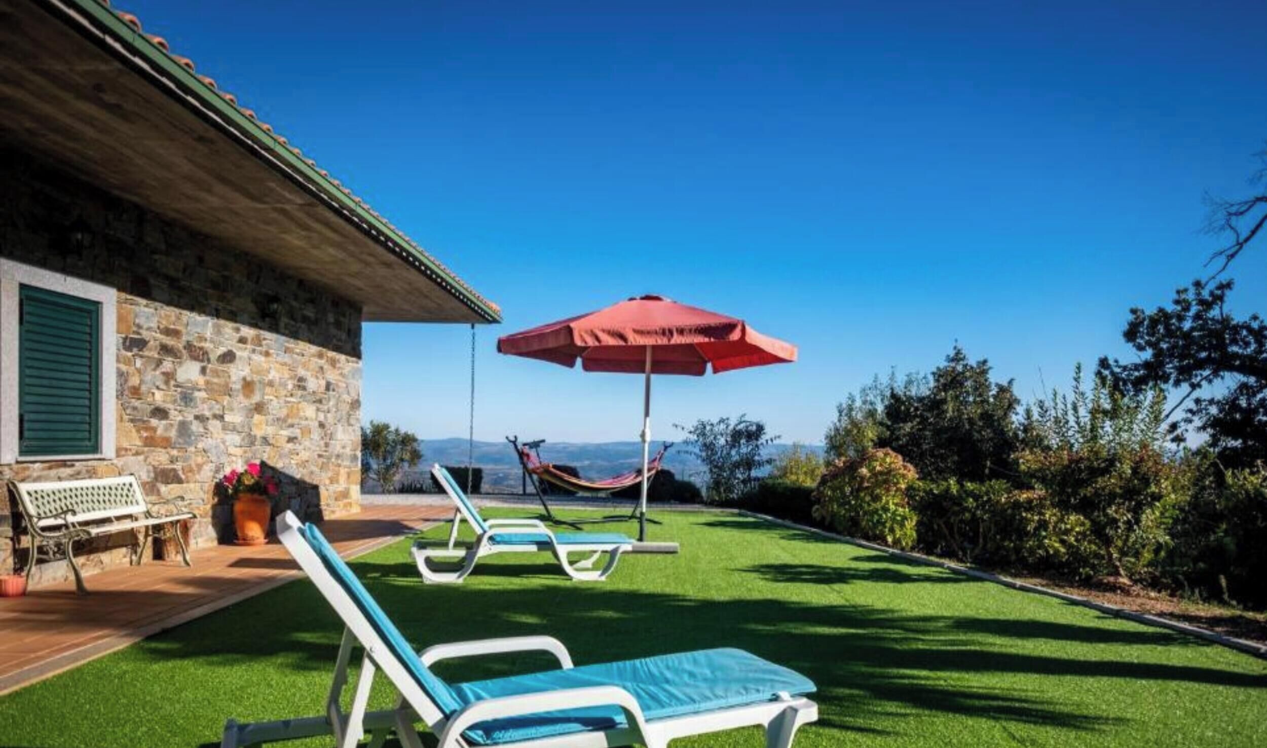 A stone building with a patio, a hammock, and lounge chairs with a red umbrella.