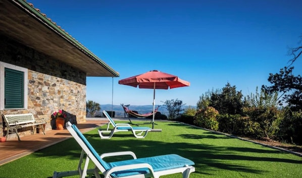 A stone building with a patio, a hammock, and lounge chairs with a red umbrella. - MyStay - Pereira Soeima House (Macedo de cavaleiros)
