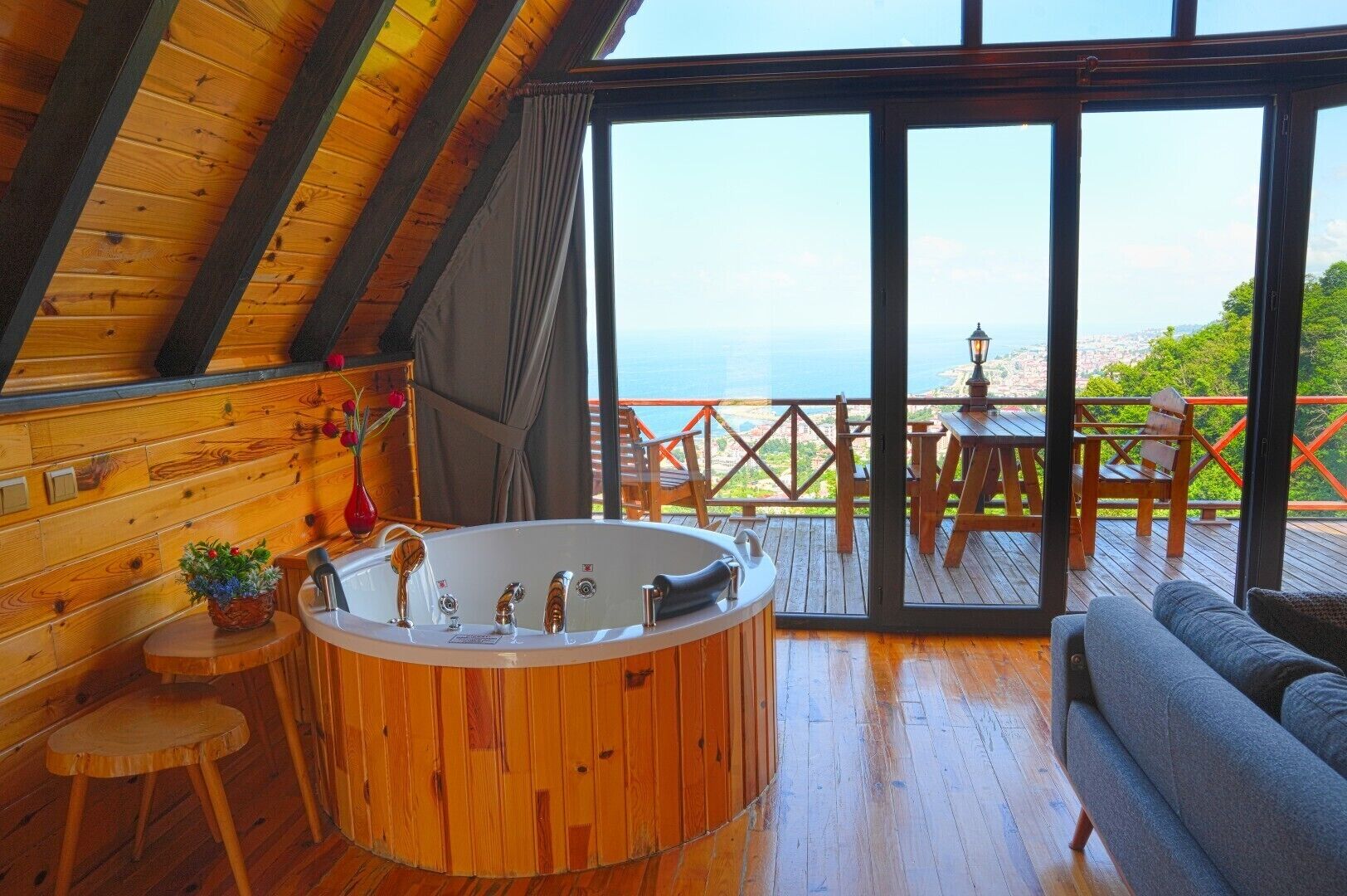 A wooden interior with a hot tub, a sofa, and a view of the sea.