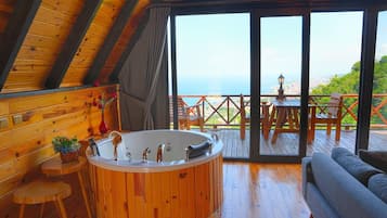 A wooden interior with a hot tub, a sofa, and a view of the sea.