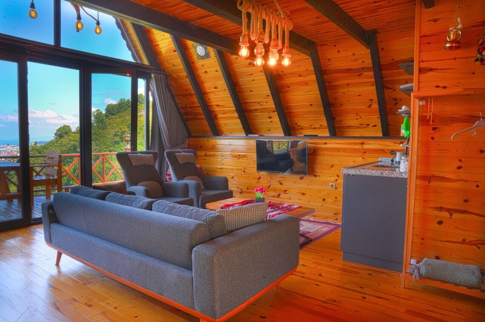Une pièce mansardée avec un canapé, des fauteuils, un téléviseur et un plafond en bois.