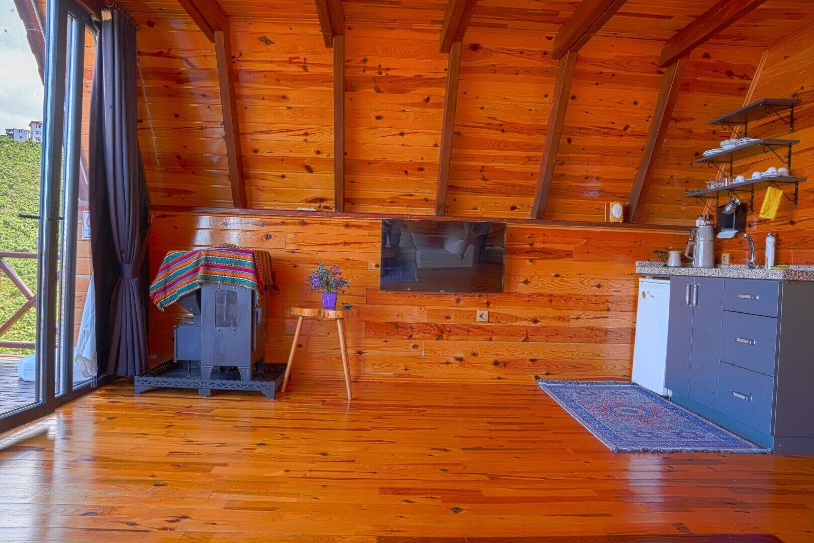 A wooden cabin interior with a fireplace, a television, and a kitchen area.