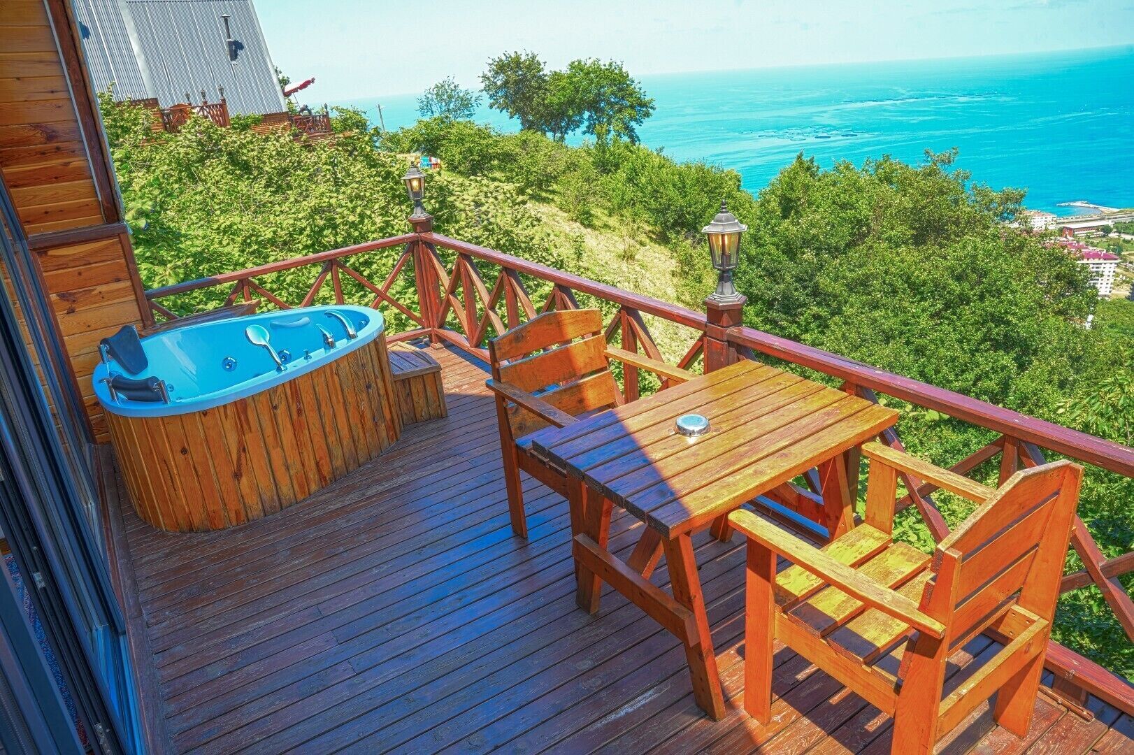 Terraza de madera con jacuzzi, mesa y sillas, con vista al mar.