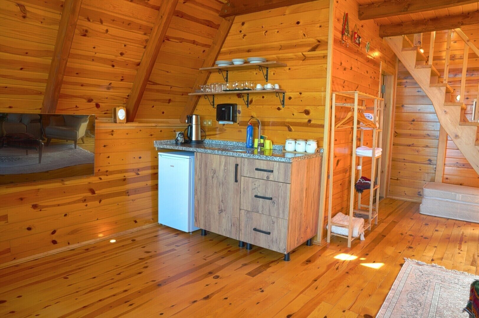 L’intérieur d’un chalet en bois comprend un coin cuisine, une table à manger et un escalier.
