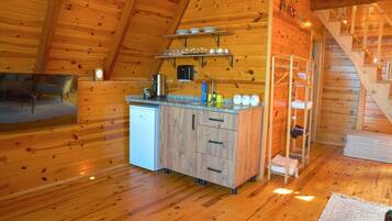 L’intérieur d’un chalet en bois comprend un coin cuisine, une table à manger et un escalier.