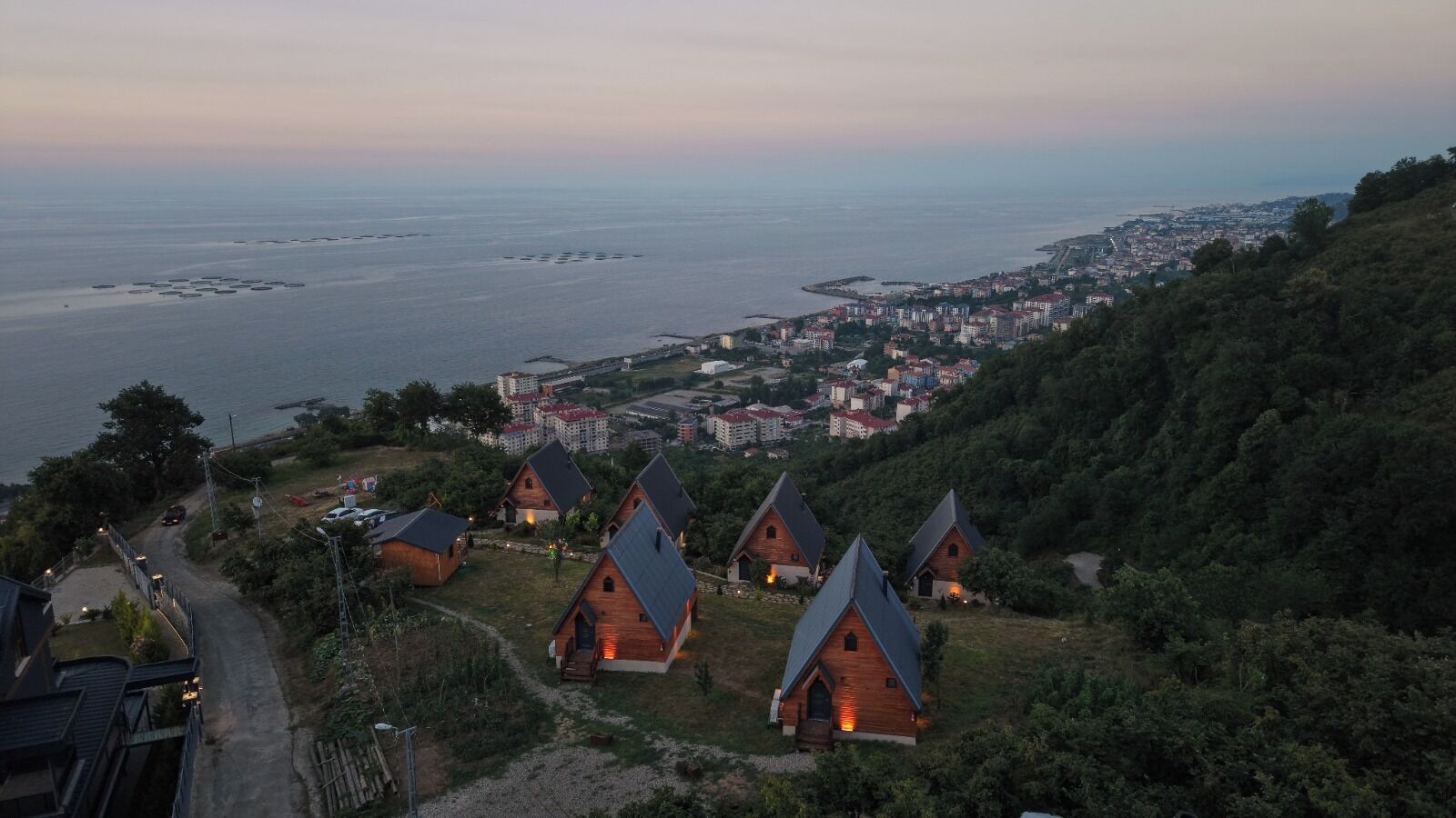 A coastal village with traditional houses, a road, and a view of the sea and distant city.