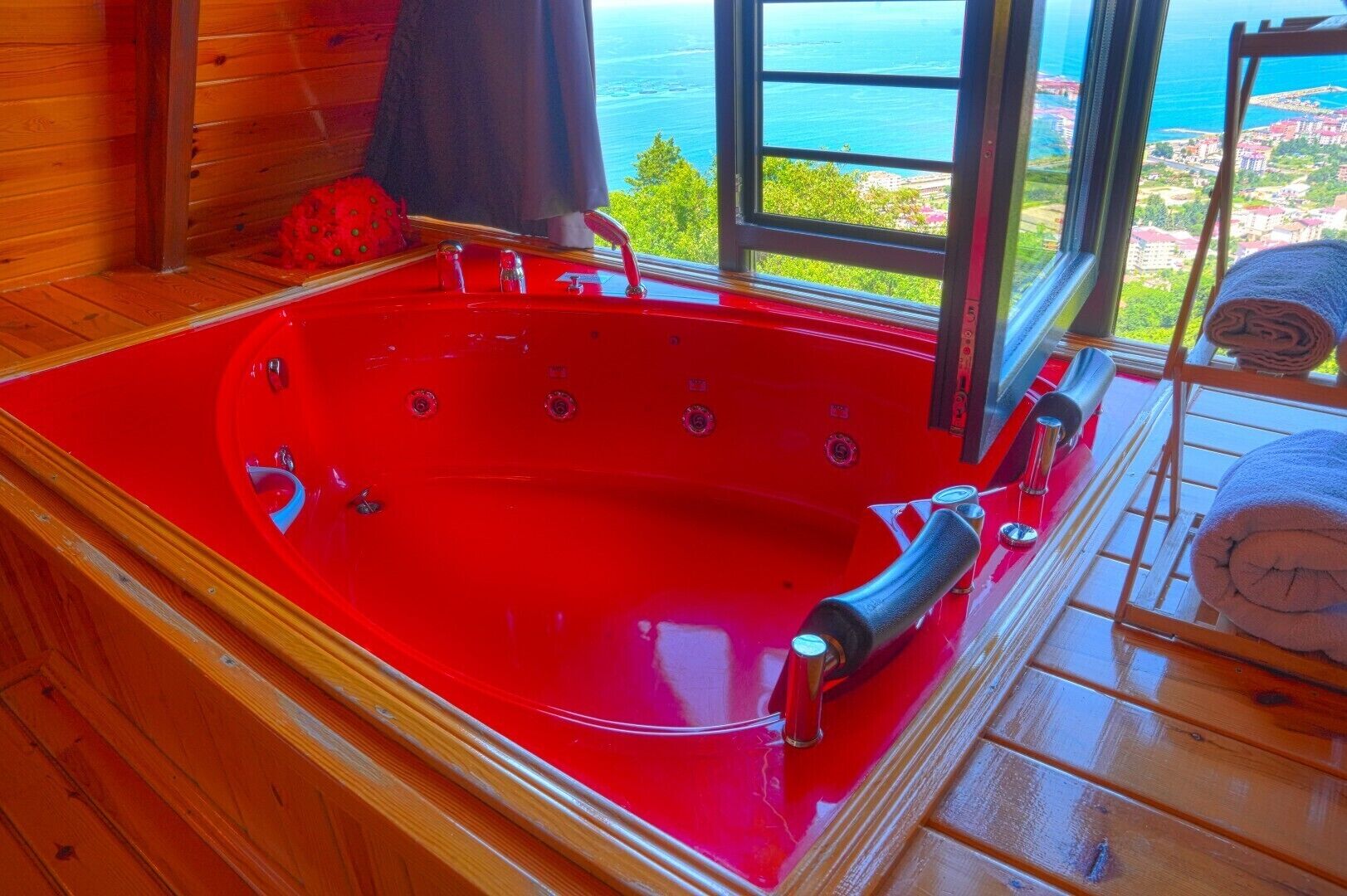 A red jacuzzi tub with a view of the sea through a window.