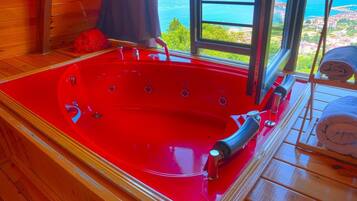 A red jacuzzi tub with a view of the sea through a window.