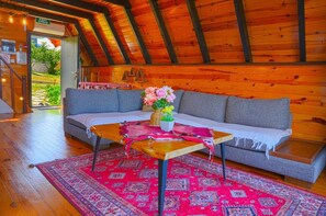 Una habitación acogedora con techo de madera, un sofá gris, una mesita con un florero y una alfombra estampada.