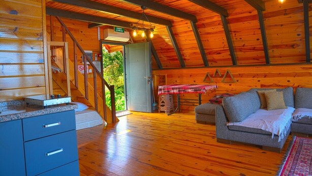 Interior d'una cabana de fusta amb unes escales de fusta, un sofà i una taula amb una manta.