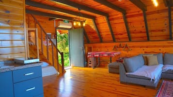 A log cabin interior with a wooden staircase, a sofa, and a table with a blanket.