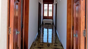 Um corredor com portas de madeira, soalho em azulejos e uma janela com vista.