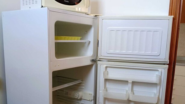 Uma geladeira branca com um micro-ondas em cima, uma garrafa de água dentro e um piso estampado.