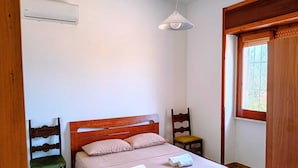 Quarto com cama de madeira, mesa de cabeceira, cadeira, luminária pendente e janela.