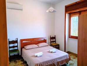 Ein Schlafzimmer mit einem hölzernen Bett, einem Nachttisch, einem Sessel, einer Pendelleuchte und einem Fenster.