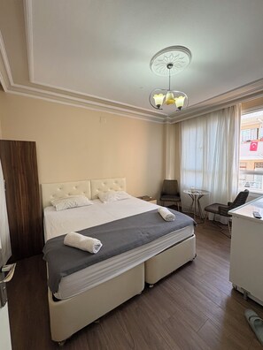 A hotel room with a large bed, a desk, a chair, a small table, and a view of the outside. - Kerem dalgıç suit (Adana)