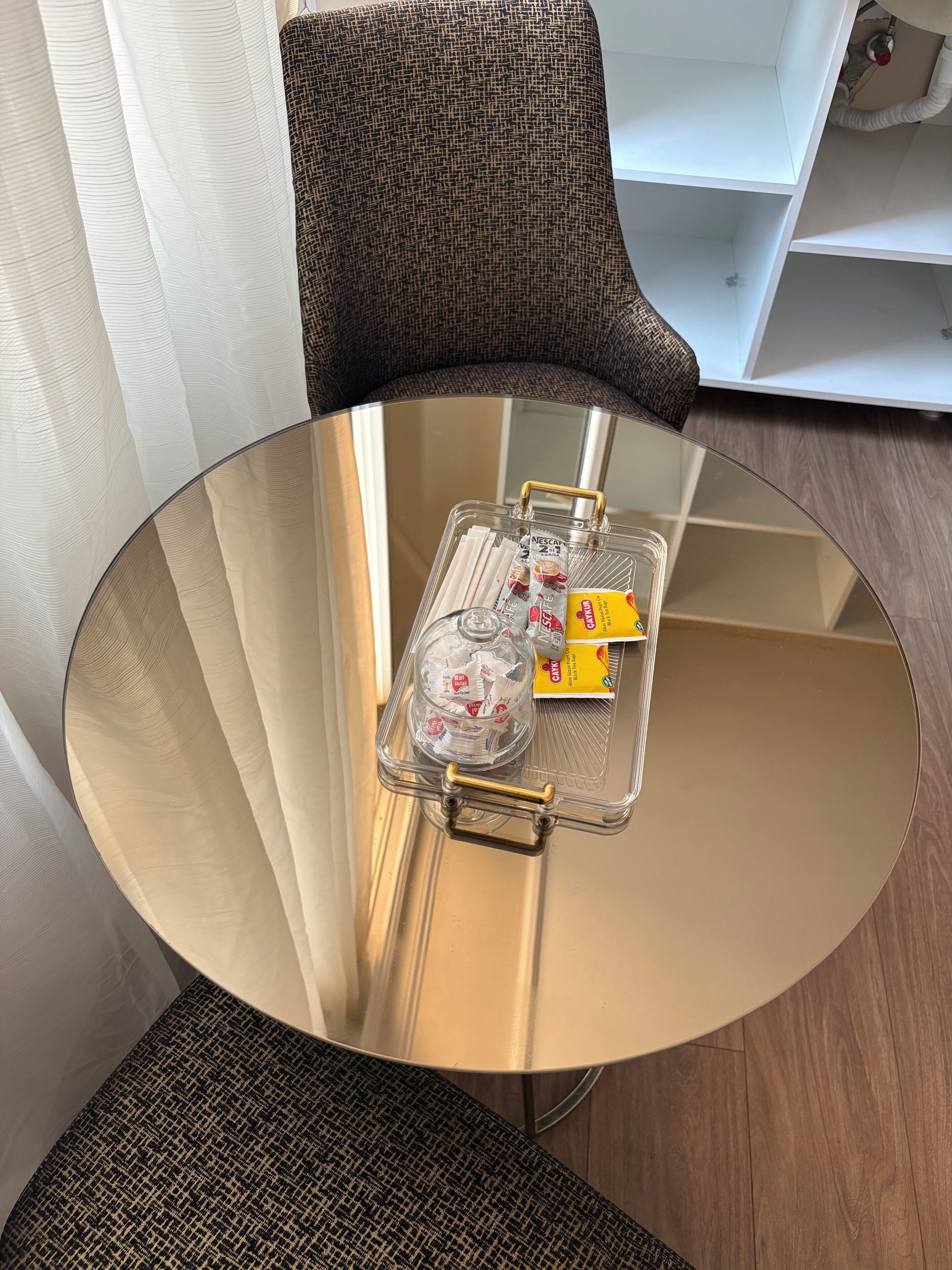 A round glass table with a clear plastic tray containing a bottle, a glass, and a yellow box.