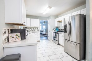 Una cocina moderna con armarios blancos, un refrigerador de acero inoxidable y piso de baldosas.