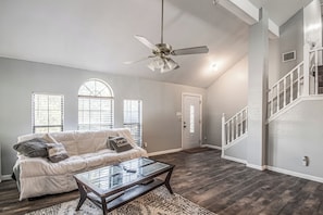 A spacious living room with a white sofa, a glass coffee table, and a ceiling fan.