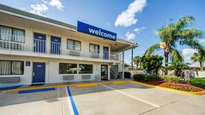Un hotel con un cartel de 'Welcome', un estacionamiento y un edificio con varios balcones.