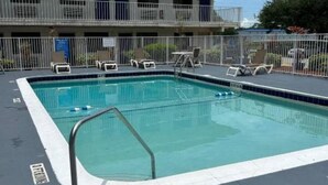 Piscina com espreguiçadeiras e um edifício com várias portas ao fundo.