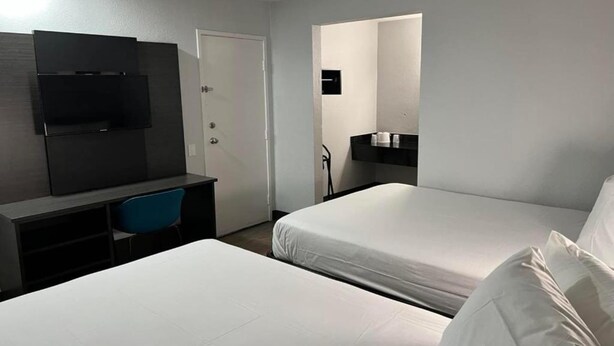 Hotellihuone, jossa on kaksi sänkyä, työpöytä tuolilla, televisio ja pieni kylpyhuone.