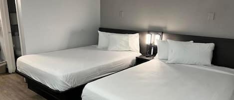 Ein Hotelzimmer mit zwei Einzelbetten, einem Nachttisch mit Lampe und einer Tür zu einem Badezimmer.