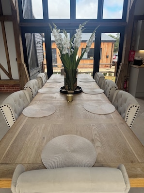 A dining table with a vase of white flowers, surrounded by upholstered chairs with studded backs. - Barn - Sleeps 10 - Hot Tub - Parking (Reigate)