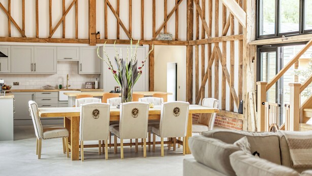 Een eetgedeelte met een houten tafel en stoelen, een vaas met bloemen, en een keuken op de achtergrond.