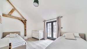 Een slaapkamer met twee bedden, een wieg, een raam met gordijnen en een houten balk.