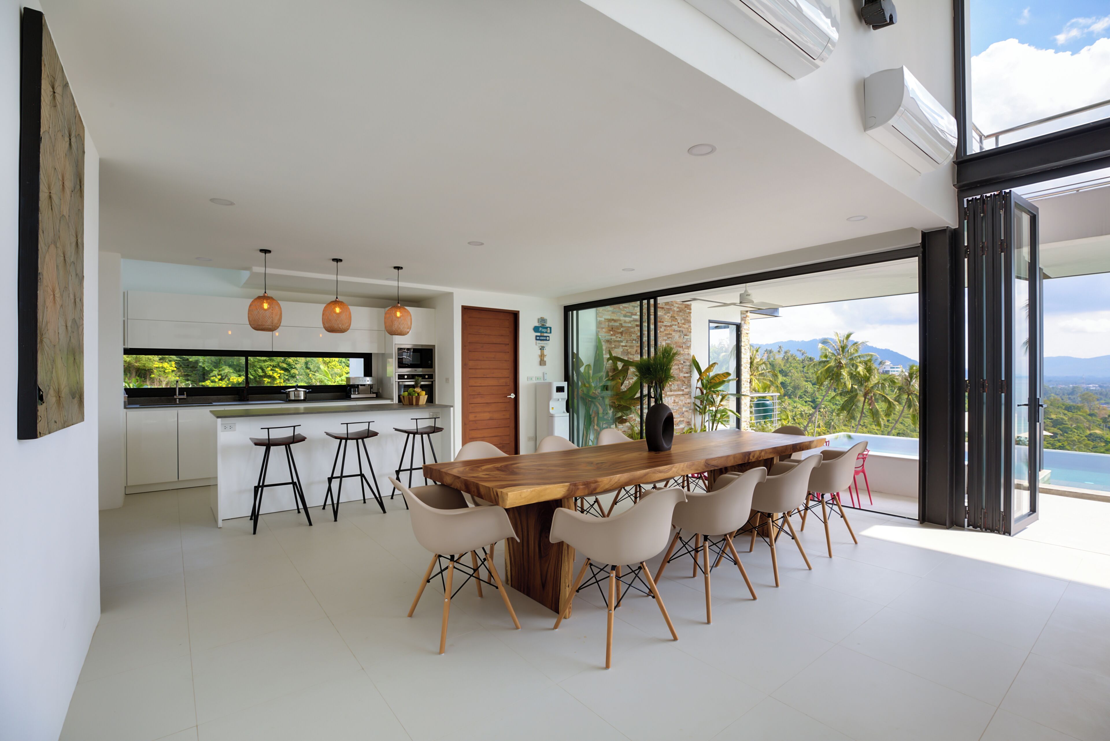 A modern kitchen with bar stools, a wooden dining table, and a view of the outdoors.
