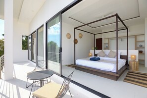 Une chambre moderne avec un lit à baldaquin, un balcon doté d’une table et de chaises, et une grande porte-fenêtre coulissante.