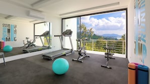 A modern gym with exercise equipment, a large window with a view of palm trees and mountains, and a wall with motivational text.