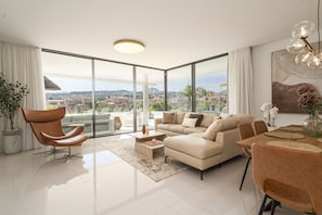 A modern living room with a sofa, chairs, a coffee table, and a dining area with a table and chairs. - Cateleya Residence by Time & Home (Estepona)