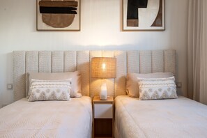 A double bed with a textured headboard, two bedside tables with lamps, and decorative pillows. - Cateleya Residence by Time & Home (Estepona)