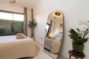 Ein Schlafzimmer mit einem großen Bett, einem Spiegel, einer Zimmerpflanze und Blick ins Freie.