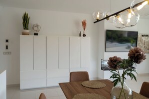 Ein zeitgemäßer Essbereich mit einem weißen Schrank, einem Holztisch und einer Vase mit Blumen.