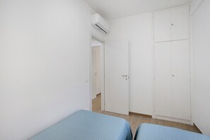 Een eenvoudige kamer, schaars ingericht, met een enkel bed, een kledingkast en een airconditioning.