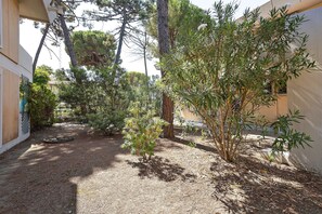 A courtyard with a variety of trees and shrubs, a gravel path, and a building with a white exterior. - Holiday Home 'Baby' with Private Terrace, Wi-Fi and Air Conditioning (Principina a Mare)
