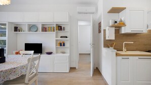 A modern kitchen with white cabinetry, a wooden countertop, and a built-in oven. There is a dining area with a table and chairs, and a bookshelf filled with books. - Holiday Home 'Baby' with Private Terrace, Wi-Fi and Air Conditioning (Principina a Mare)